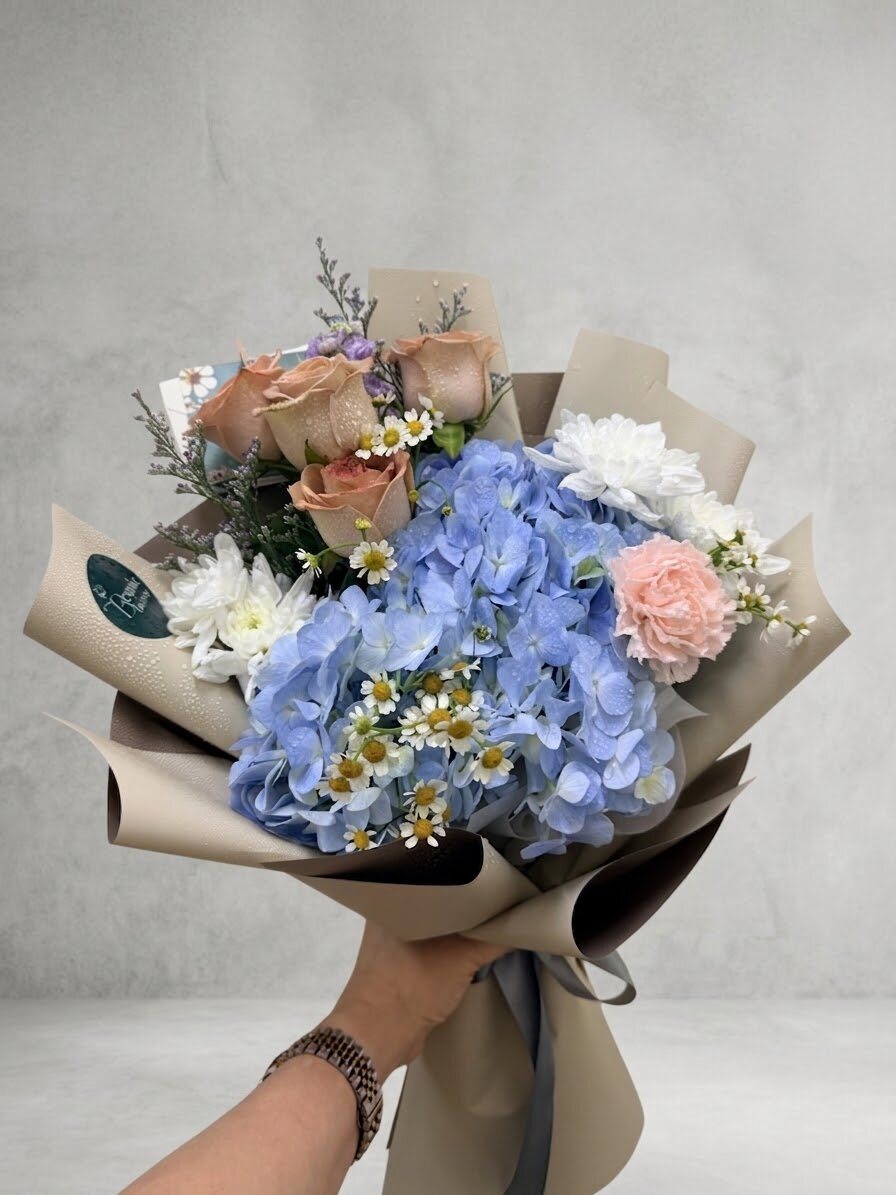Madeira - blue hydrangea with cream roses in a white wrap, held to camera