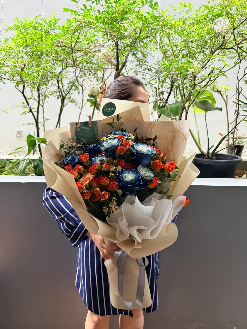 A hand-wrapped bouquet of blue and orange roses with white chamomile in kraft paper.