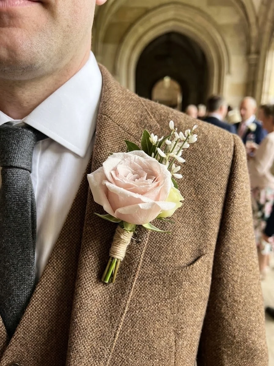 Blush rose boutonniere pinned to a tweed jacket lapel